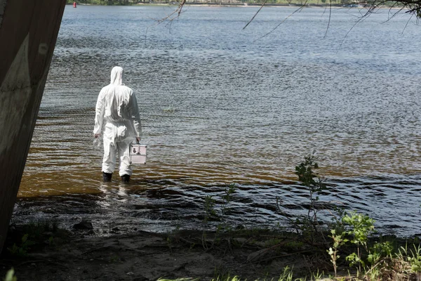 Back view of water inspector in protective costume holding inspection kit in river — Stock Photo