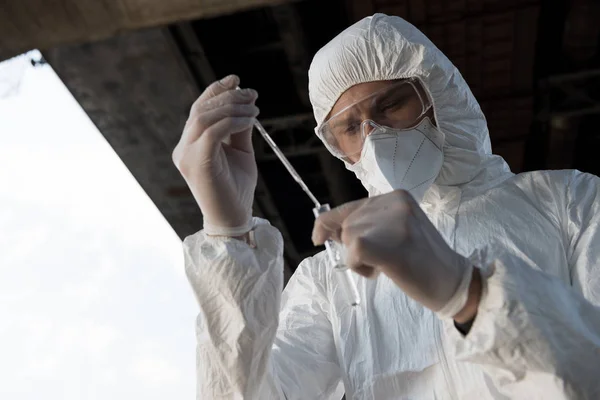 Selective focus of water inspector in protective costume, respirator and goggles taking water sample — Stock Photo