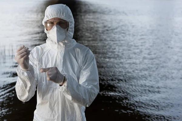 Inspector de agua en traje de protección, gafas y respirador tomando la muestra de agua en el río - foto de stock