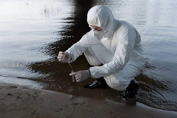 Inspector de agua en traje de protección y respirador tomando muestra de agua en el río - foto de stock