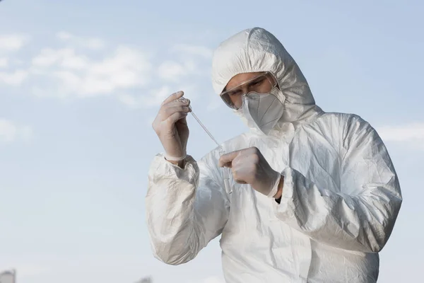 Water inspector in protective costume and respirator holding test tube with water sample — Stock Photo