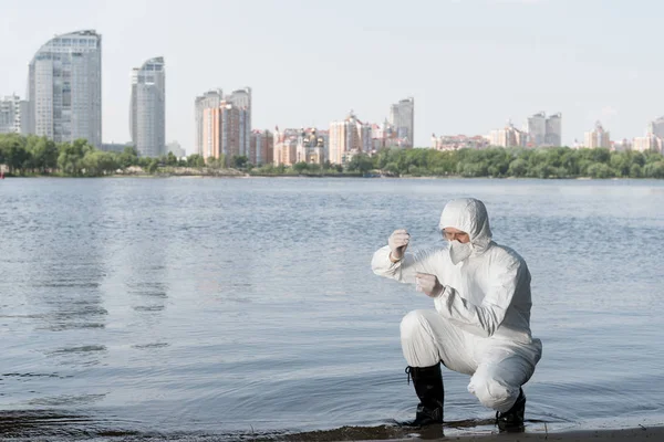 Inspector de agua en traje de protección y respirador tomando muestra de agua en el río - foto de stock