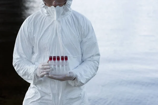 Partial view of water inspector in protective costume holding test tubes — Stock Photo