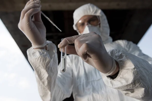 Selective focus of water inspector in protective costume and respirator taking water sample — Stock Photo