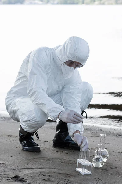 Water inspector in protective costume and respirator taking water samples at river — Stock Photo