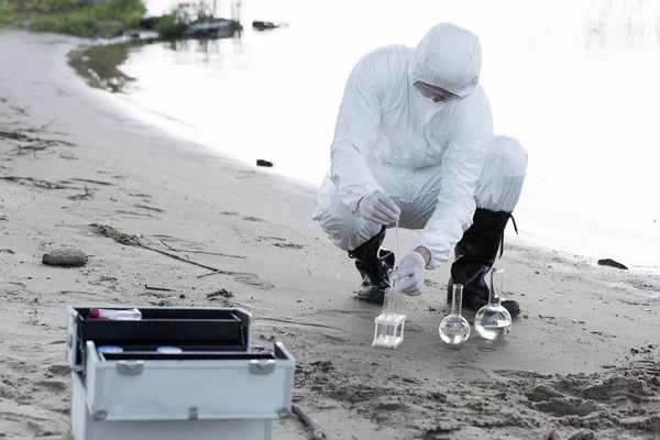 Inspecteur de l'eau en costume de protection et respirateur prélever des échantillons d'eau à la rivière — Photo de stock