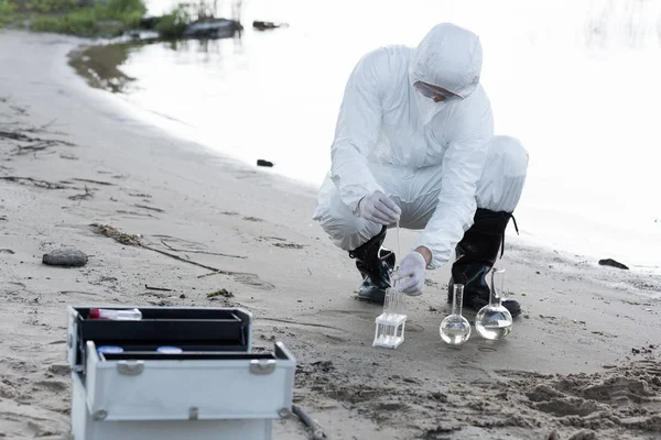 Wasserinspektor in Schutzanzügen und Atemschutzmaske entnimmt Wasserproben am Fluss — Stockfoto