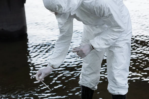 Vista recortada del inspector de agua en guantes de látex tomando muestra de agua en el río - foto de stock