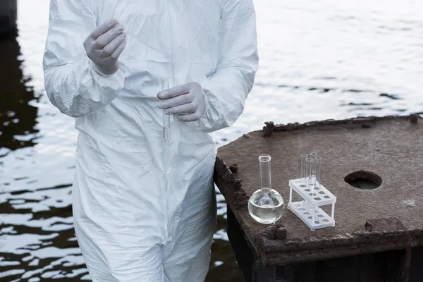 Vista recortada del inspector de agua en guantes de látex tomando muestras de agua en el río - foto de stock