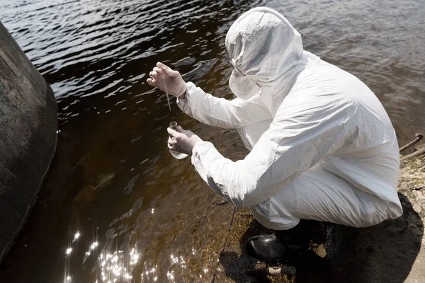 Water inspector in protective costume, latex gloves and respirator taking water sample at river — Stock Photo