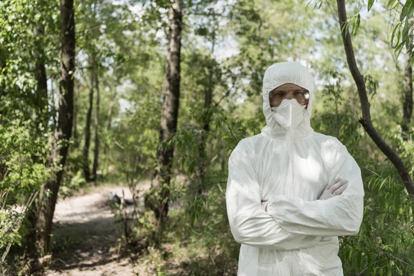 Vorderansicht des Ökologen in Schutzkleidung und Atemschutzmaske mit verschränkten Armen im Wald — Stockfoto