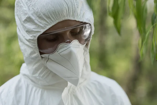 Ecologist in protective costume, goggles and respirator looking down — Stock Photo