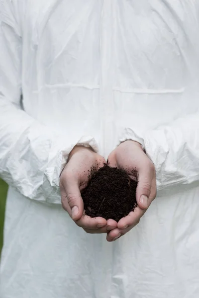 Partial view of ecologist in protective costume holding handful of soil — Stock Photo