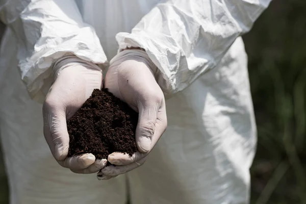 Vista parcial del ecologista en guantes de látex sosteniendo un puñado de tierra - foto de stock