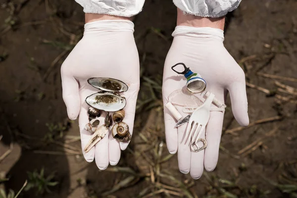 Vista recortada de ecologista en guantes de látex sosteniendo basura plástica y - foto de stock