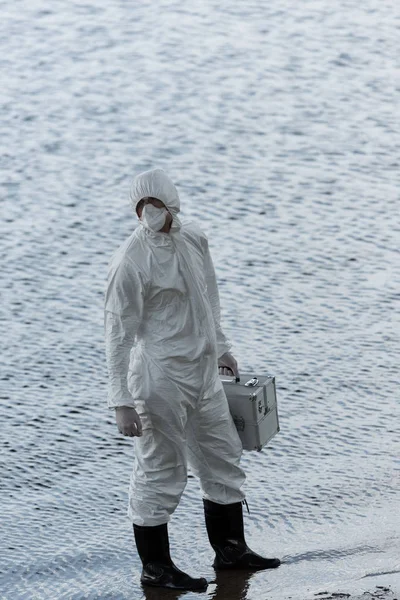 Full length view of water inspector in protective costume holding inspection kit at river — Stock Photo