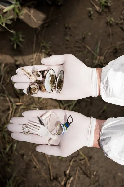 Cropped view of ecologist in latex gloves holding seashells and plastic garbage — Stock Photo