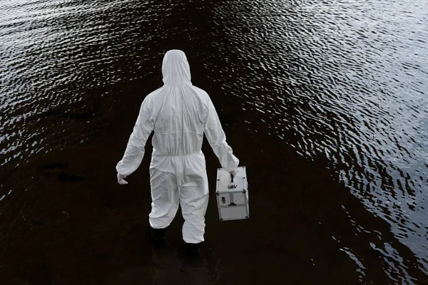 Back view of water inspector in protective costume holding inspection kit in river — Stock Photo
