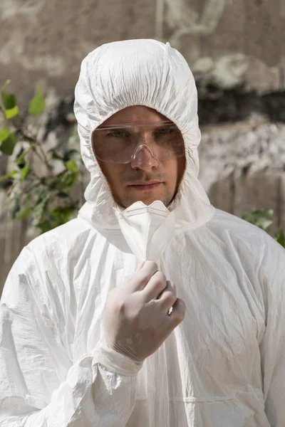 Front view of ecologist in protective costume and goggles taking off respirator — Stock Photo