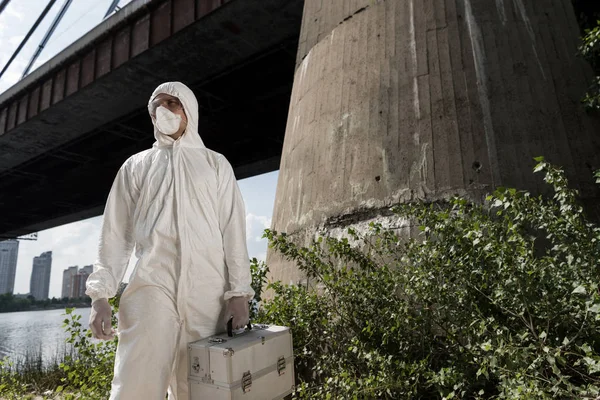 Ecologist in protective costume with inspection kit standing near bridge — Stock Photo