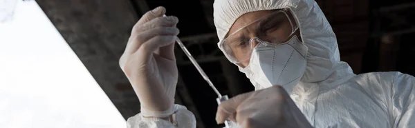 Panoramic shot of water inspector in respirator and goggles taking water sample — Stock Photo