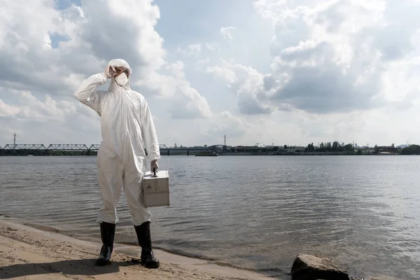 Full length view of water inspector in protective costume holding inspection kit at river coast — Stock Photo