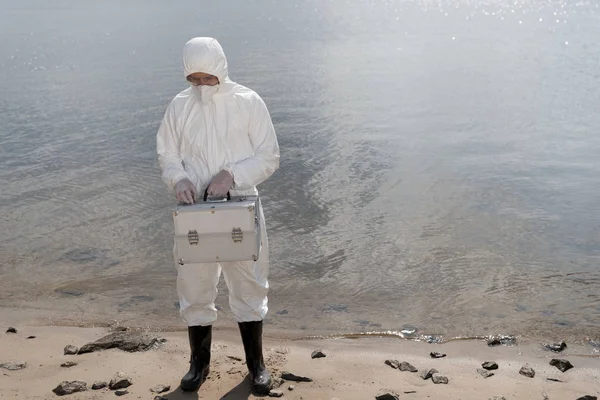 Full length view of water inspector in protective costume holding inspection kit at river coast — Stock Photo