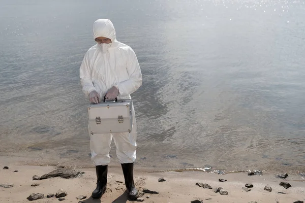 Vista completa del inspector de agua en traje de protección que sostiene el kit de inspección en la costa del río - foto de stock