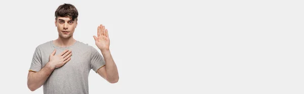 Панорамний знімок впевненого молодого чоловіка, що показує жест лаятися на камеру ізольовано на сірому — стокове фото