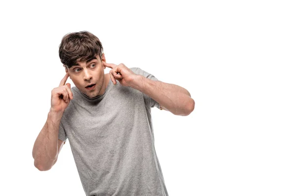 Scared young man looking away while plugging ears with hands isolated on white — Stock Photo