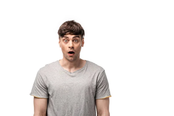 Шокированный молодой человек в серой футболке, смотрящий на камеру, изолированную на белом — стоковое фото