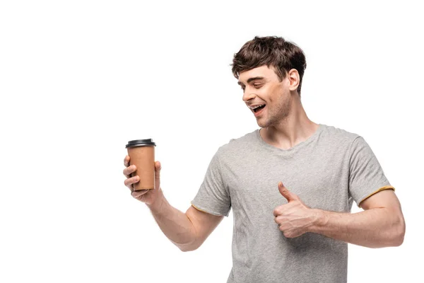 Улыбающийся красивый мужчина смотрит на одноразовую чашку и показывает большой палец на белом — стоковое фото