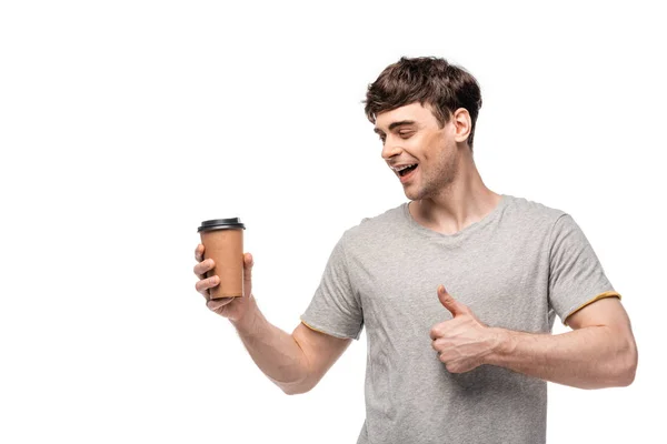 Sourire bel homme regardant la tasse jetable et montrant pouce vers le haut isolé sur blanc — Photo de stock