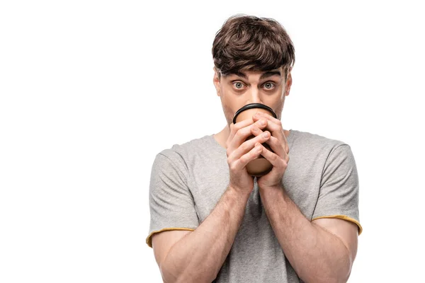 Shocked young man drinking coffee to go while looking at camera isolated on white — Stock Photo