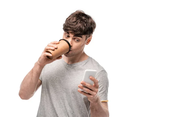 Красивий молодий чоловік використовує смартфон під час пиття кави, щоб піти ізольовано на білому — стокове фото