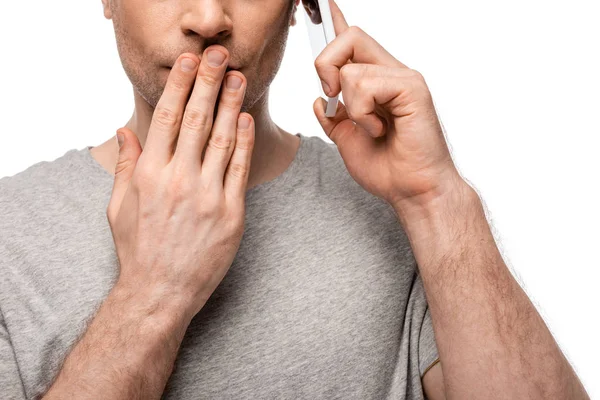 Vista recortada del hombre que cubre la boca con la mano mientras habla en el teléfono inteligente aislado en blanco - foto de stock