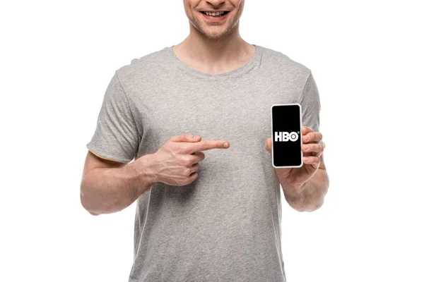 KYIV, UCRANIA - 16 de mayo de 2019: vista recortada del hombre sonriente apuntando al teléfono inteligente con la aplicación HBO, aislado en blanco - foto de stock