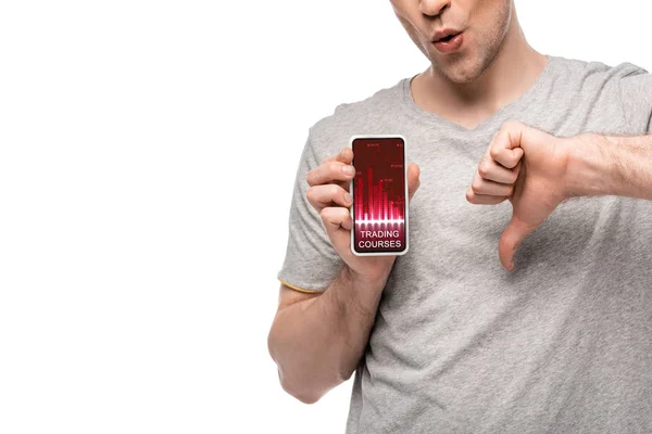 Vista recortada del hombre que muestra el pulgar hacia abajo y el teléfono inteligente con la aplicación de cursos de comercio, aislado en blanco - foto de stock