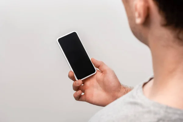 Обрізаний вид людини, що тримає смартфон з порожнім екраном ізольовано на сірому — стокове фото