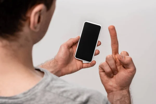 Vue en cuivre de l'homme montrant le majeur tout en tenant smartphone avec écran vide isolé sur gris — Photo de stock