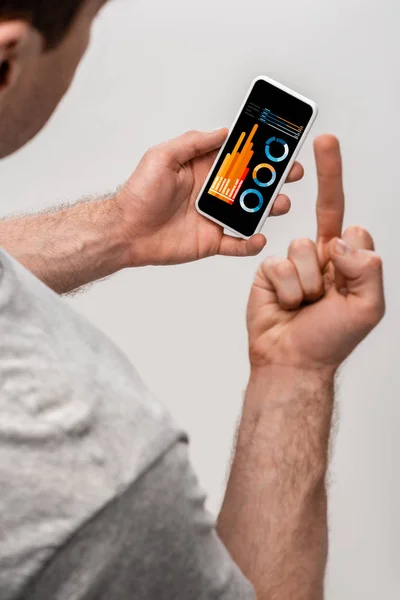 Cropped view of man using smartphone with infographic app and showing middle finger, isolated on grey — Stock Photo