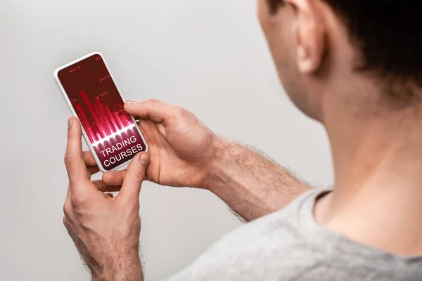 Обрезанный вид человека с помощью смартфона с приложением торговых курсов, изолированный на серый — стоковое фото