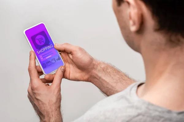 Обрезанный вид человека с помощью смартфона с приложением для покупок, изолированный на сером — стоковое фото