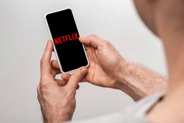 KYIV, UKRAINE - 16 MAI 2019 : vue recadrée de l'homme à l'aide d'un smartphone avec application netflix, isolé sur gris — Photo de stock