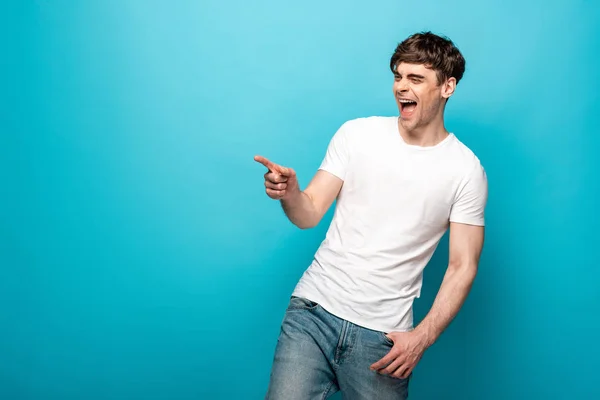 Lachender Mann, der mit dem Finger zeigt, während er auf blauem Hintergrund wegschaut — Stockfoto