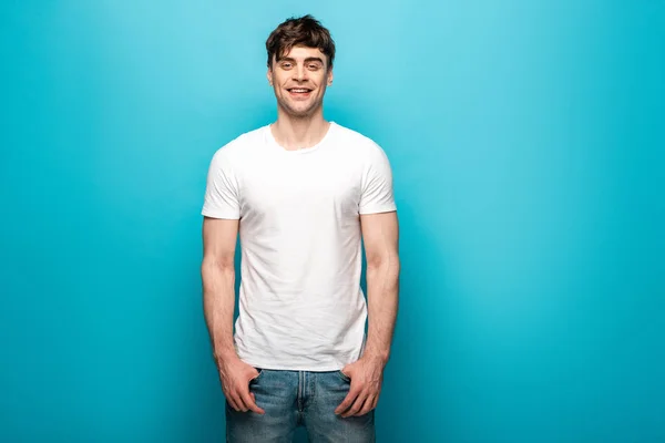 Handsome young man in white t-shirt smiling at camera on blue background — Stock Photo