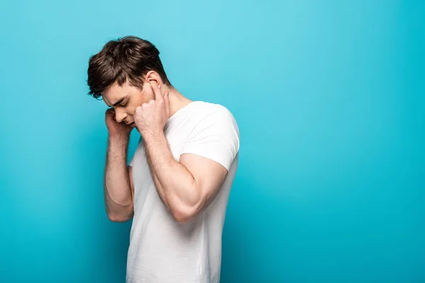 Erschöpfter junger Mann stopft Ohren mit Fingern auf blauem Hintergrund — Stockfoto