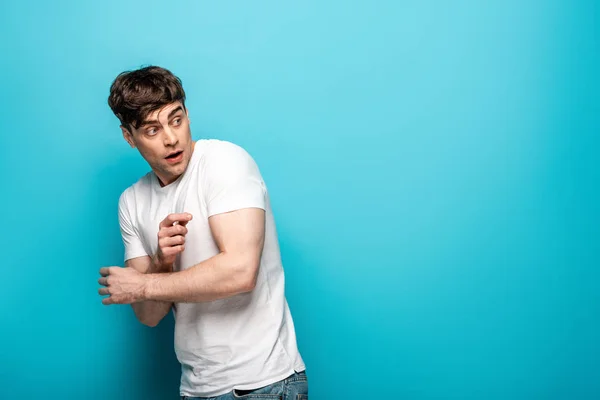 Frightened young man in white t-shirt looking back on blue background — Stock Photo