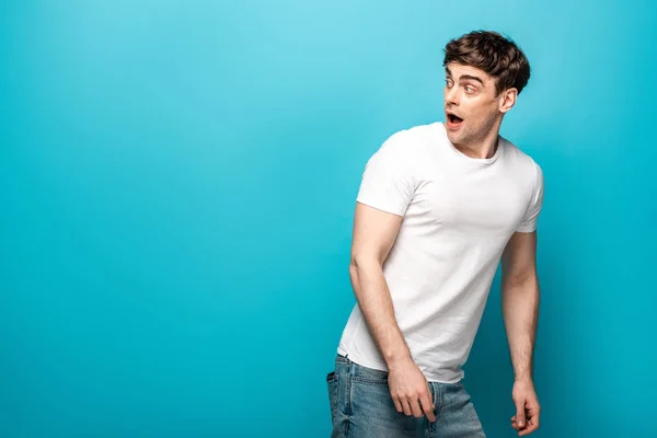 Scared young man in white t-shirt looking back on blue background — Stock Photo