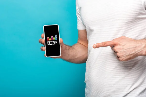 KYIV, UKRAINE - MAY 16, 2019: cropped view of man pointing at smartphone with deezer app, isolated on blue — Stock Photo